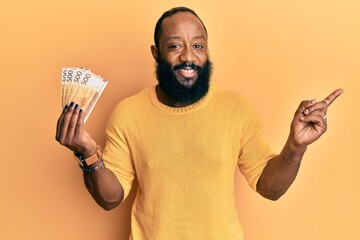 Young african american man holding 500 norwegian krone banknotes smiling happy pointing with hand...