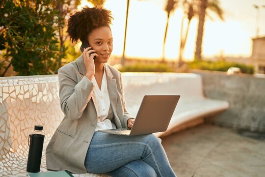 Young african american businesswoman working using laptop sitting and talking on the smartphone.