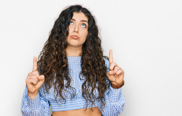 Young hispanic girl wearing casual clothes pointing up looking sad and upset, indicating direction...