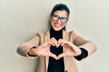 Young hispanic woman wearing business style and glasses smiling in love showing heart symbol and...