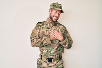 Young caucasian man wearing camouflage army uniform smiling with hands on chest with closed eyes and grateful gesture on face. health concept.