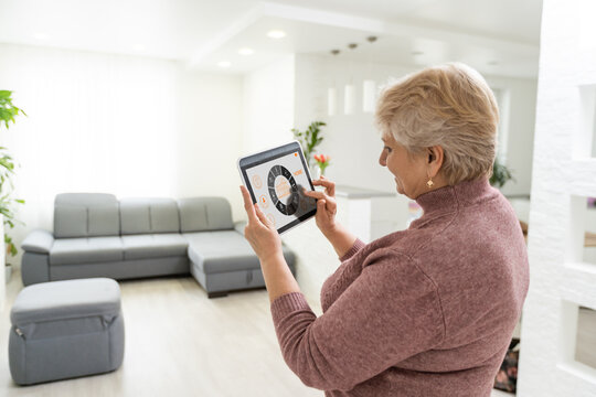 technology, automation and efficiency concept - smiling senior woman in glasses with tablet computer using smart home app over grey background - Powered by Adobe