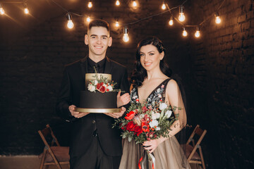 Fototapeta na wymiar Wedding of a beautiful couple in a black dress, a bouquet of marsala color, at a festive table with candles and a cake against a black wall
