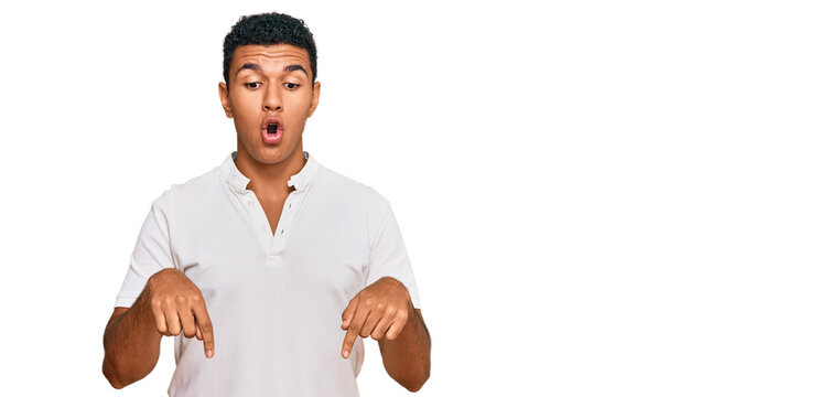 Young arab man wearing casual clothes pointing down with fingers showing advertisement, surprised face and open mouth