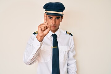 Young hispanic man wearing airplane pilot uniform pointing with finger up and angry expression, showing no gesture