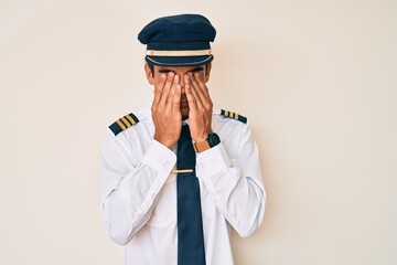 Young hispanic man wearing airplane pilot uniform rubbing eyes for fatigue and headache, sleepy and...