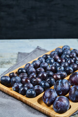 Garden plums on wooden platter and on dark background