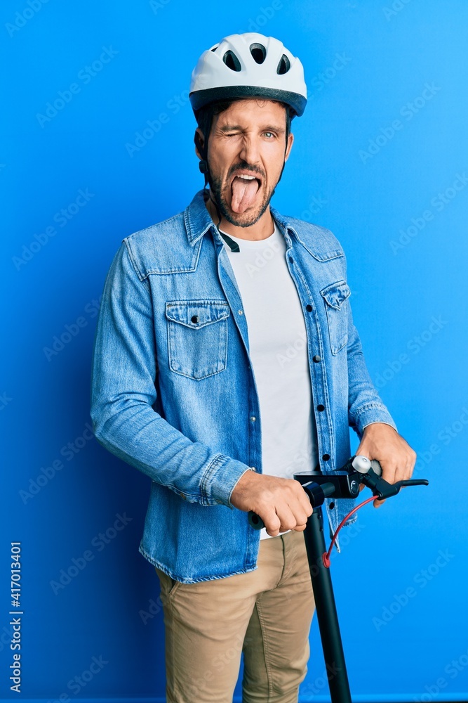 Sticker Young handsome man standing on modern scooter wearing helmet sticking tongue out happy with funny expression.