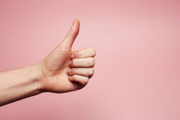 Like gesture — woman's hand with thumb up demonstrates approval or agreement solated on the bright solid pink fond background