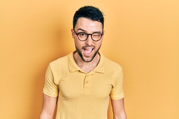 Young hispanic man wearing casual clothes and glasses winking looking at the camera with sexy expression, cheerful and happy face.