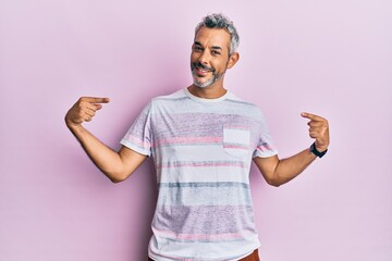 Middle age grey-haired man wearing casual clothes looking confident with smile on face, pointing...