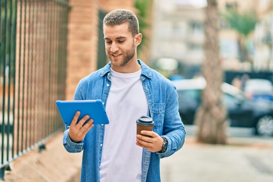 Young caucasian man smiling happy using touchpad and drinking coffee at the city.