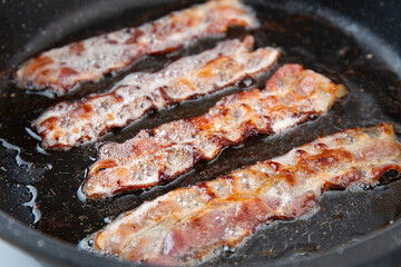 Crispy smokey bacon slice or strip. Unhealthy fat food, fattenig ingredient. Red Thin slice or strip or rashers of bacon is fried in a pan, pork fat is melted. High calorie food. Idea for breakfast