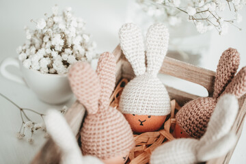 Cute Easter eggs in crocheted hats with bunny ears in a wooden box on the table Home happy easter decoration concept.