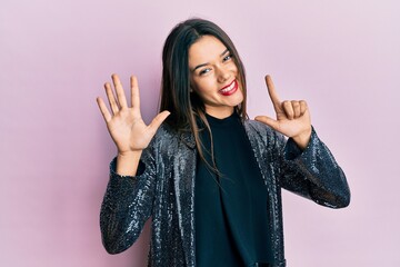 Young hispanic girl wearing party jacket showing and pointing up with fingers number seven while...