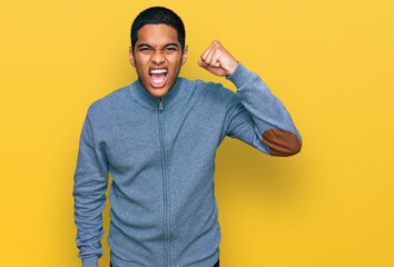 Young handsome hispanic man wearing casual sweatshirt angry and mad raising fist frustrated and...
