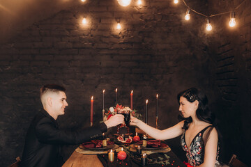 Wedding of a beautiful couple in a black dress, a bouquet of marsala color, at a festive table with candles and a cake against a black wall