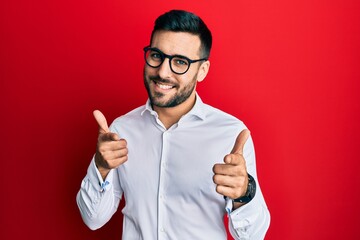 Young hispanic businessman wearing shirt and glasses pointing fingers to camera with happy and funny face. good energy and vibes.