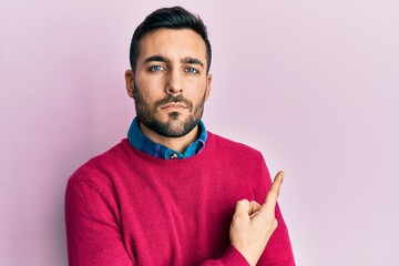 Young hispanic man wearing casual clothes pointing with hand finger to the side showing advertisement, serious and calm face