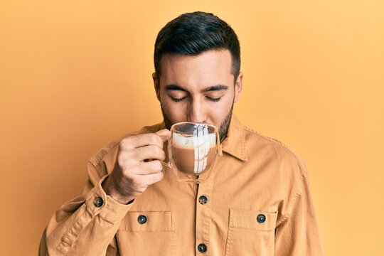 Handsome hispanic man enjoying a cup of coffee over yellow background