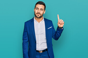 Young hispanic man wearing business jacket showing and pointing up with finger number one while...