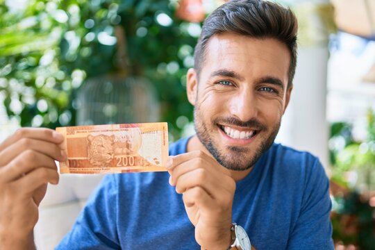Young hispanic man smiling happy holding one south african rand banknote at the terrace.