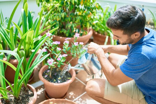 Young handsome man smiling happy caring plants using watering can at terrace