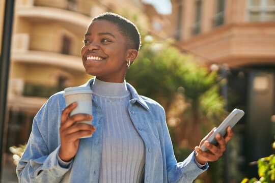 Young african american woman using smartphone and drinking coffee at the city