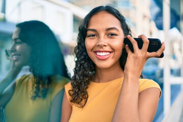 Young african american girl listening audio message using smartphone at city.