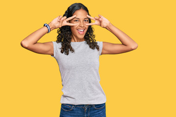 Young african american girl wearing casual clothes doing peace symbol with fingers over face, smiling cheerful showing victory