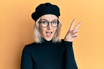Young blonde girl wearing french look with beret smiling with happy face winking at the camera...