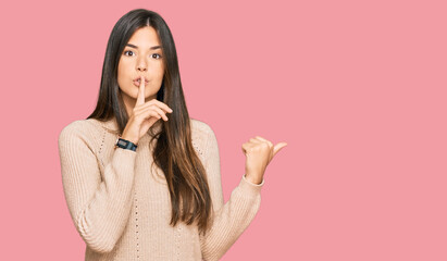Young brunette woman wearing casual winter sweater asking to be quiet with finger on lips pointing with hand to the side. silence and secret concept.