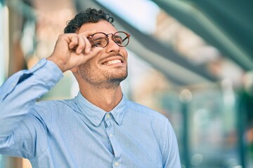 Young hispanic businessman smiling happy touching his glasses at the city.
