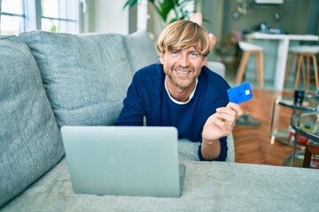 Middle age handsome caucasian man relaxing at home doing online shopping using credit card on computer laptop