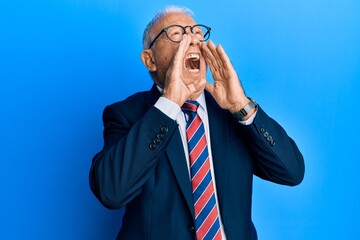 Senior caucasian man wearing business suit and tie shouting angry out loud with hands over mouth