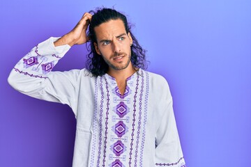 Young handsome man with long hair wearing bohemian and hippie shirt confuse and wonder about...