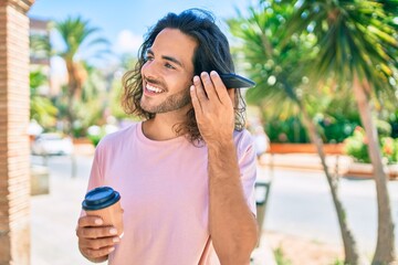 Young hispanic man smiling happy talking on the smartphone and drinking take away coffee at city.