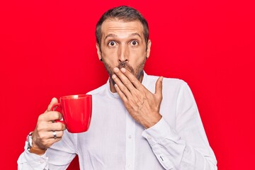 Young handsome man holding coffee covering mouth with hand, shocked and afraid for mistake. surprised expression