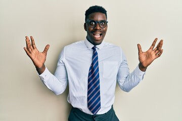 Handsome black man wearing glasses business shirt and tie celebrating crazy and amazed for success with arms raised and open eyes screaming excited. winner concept