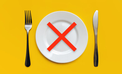 A white plate with a red cross stands on the yellow tablecloth. The concept is about intermittent fasting, diet and healing diet. Top view, white background, copy space.