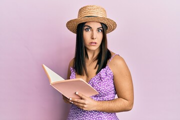 Young brunette woman reading book clueless and confused expression. doubt concept.