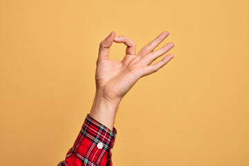 Fototapeta na wymiar Hand of caucasian young man showing fingers over isolated yellow background gesturing approval expression doing okay symbol with fingers