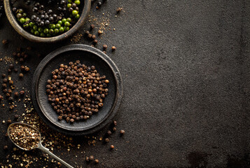 Black pepper in various forms; raw, dried and crushed peppercorns on a black background with space...