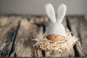 Easter egg in a crocheted hat with bunny ears in a nest on old wooden boards. Home happy easter decoration concept.