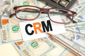 The letters CRM are written on a white card lying on the bills, glasses, pen and calculator in the background. The concept of business and Finance