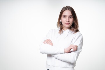 Cute young student with long fair hair is looking in a camera, standing with her hands folded, white background, studio photo