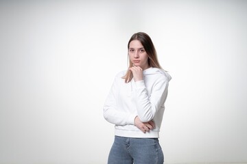 A sweet girl in her 20s with fair hair is pensive and thoughtful listening to music in her white wireless earphones, studio photo