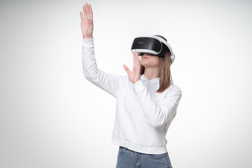 Young girl in white hoodie, wearing VR glasses and touching air as if she sees something, studio, white background