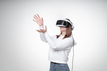 Young girl with fair hair, testing VR glasses and raises her hands up, gesturing, studio, white background