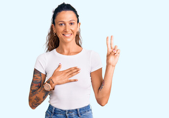 Young hispanic woman with tattoo wearing casual white tshirt smiling swearing with hand on chest...